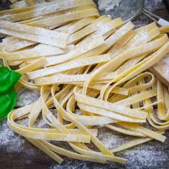 Świeży makaron tagliatelle, posypany mąką, z listkami bazylii. Idealny jako alternatywa, czym zastąpić makaron pszenny.