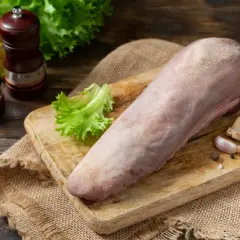Surowy ozór wieprzowy na desce, obok liść sałaty, czosnek i przyprawy. Gotowy do przygotowania pysznego dania.