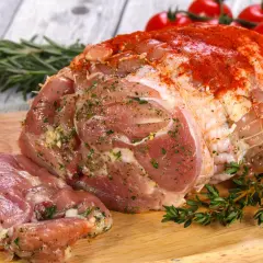 Surowa szynka z kurczaka, doprawiona ziołami i papryką, gotowa do pieczenia. Obok gałązki rozmarynu i tymianku, w tle pomidorki koktajlowe.