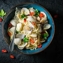 Makaron spaghetti z aromatycznymi vongole, czosnkiem i ostrą papryczką, udekorowany natką pietruszki.