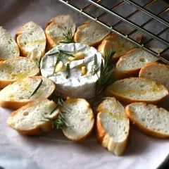 Pyszny, pieczony camembert z czosnkiem i rozmarynem, otoczony kromkami bagietki. Idealna przekąska na ciepło.