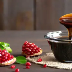 Granat i jego nasiona obok miseczki z gęstą, ciemną melasą. Co to jest melasa? To słodki syrop z owoców granatu.