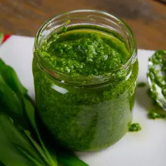 Słoik pełen aromatycznego pesto z czosnku niedźwiedziego, obok świeże liście i łyżka z porcją zielonego sosu.