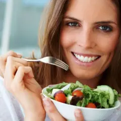 Uśmiechnięta kobieta z widelcem w dłoni, jedząca świeżą sałatkę. Idealny posiłek na diecie 1200 kcal.
