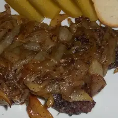 Pyszna kaszanka z patelni, duszona z cebulką, podana z ogórkiem kiszonym i kromką chleba.