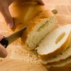 Ręka kroi świeżo upieczony chleb domowy na desce. Idealny przepis na chleb domowy pieczony w piekarniku.