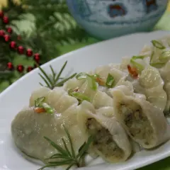 Pyszne, domowe pierogi ukraińskie, udekorowane szczypiorkiem i rozmarynem, prezentują się apetycznie na białym talerzu.
