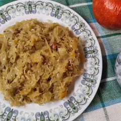 Na talerzu z ozdobnym wzorem znajduje się porcja pysznej, **kapusty kiszonej gotowanej**. Obok jabłko i moździerz z pieprzem.
