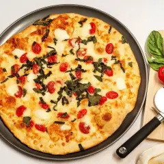 Pyszna pizza z serka wiejskiego, pomidorkami koktajlowymi i bazylią. Obok leży nóż do pizzy i świeże pomidory.