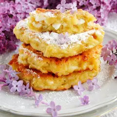 Fit placuszki z serka wiejskiego i banana, posypane cukrem pudrem, ozdobione fioletowymi kwiatami bzu.