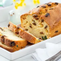 Keks ze starym przepisem, pokrojony na kromki, z bakaliami i kandyzowanymi owocami. Na talerzu obok leży nóż.