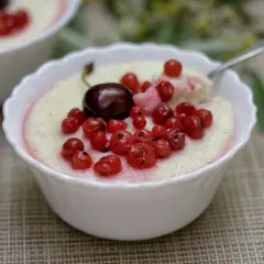 Pyszna kasza manna na mleku z wiśnią i porzeczkami, podana w białej miseczce. Idealne śniadanie lub deser.