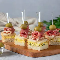 Mini kanapki z szynką, jajkiem i oliwkami na drewnianej desce. Idealne, tanie przekąski na imprezę, które zachwycą gości.