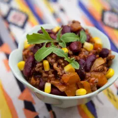 Miseczka pełna aromatycznego chili con carne przepis oryginalny, z fasolą, kukurydzą i mięsem mielonym, ozdobiona świeżymi ziołami.
