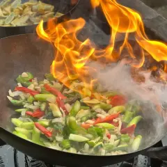 Ogień buchający z woka podczas przygotowywania pysznego stir fry z warzywami.