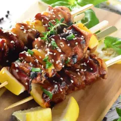 Aromatyczne yakitori z kurczaka, polane sosem teriyaki, posypane sezamem i szczypiorkiem, podane z cytryną na desce.