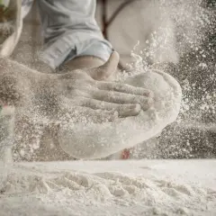 Ręce formują ciasto, a wokół unosi się chmura mąki na pizzę.