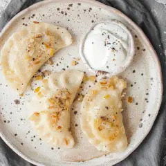 Jak odgrzać pierogi w mikrofali? Na talerzu ułożone pierogi z cebulką i śmietaną, gotowe do szybkiego podgrzania.
