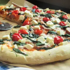 Pyszna pizza ze szpinakiem, pomidorkami koktajlowymi i kostkami sera feta. Idealna na szybki obiad.