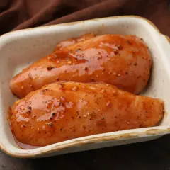 Dwie soczyste piersi z kurczaka w aromatycznym, pomarańczowym sosie, gotowe do pieczenia.