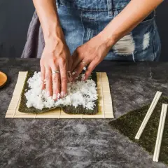 Dłonie rozprowadzają ryż na nori, przygotowując zaprawę do sushi na 500g ryżu. Obok leżą pałeczki i marynowany imbir.