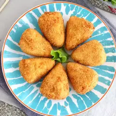 Siedem chrupiących kawałków camembert w panierce ułożonych na talerzu z niebieskimi wzorami.