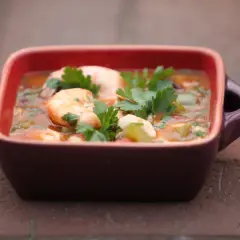 Gęste, aromatyczne gumbo z krewetkami i natką pietruszki w bordowej miseczce na ceglanej powierzchni.
