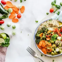 Kolorowa miska pełna warzyw i kaszy, idealna na dietę 1500 kcal. Obok świeże składniki: cukinia, marchewka, pomidorki, brukselka, limonka.