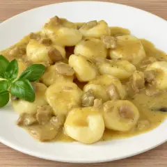 Kluski śląskie z sosem grzybowym i kawałkami mięsa, udekorowane listkiem bazylii. Pyszne danie obiadowe.