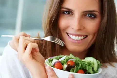 Uśmiechnięta kobieta z widelcem w dłoni, jedząca świeżą sałatkę. Idealny posiłek na diecie 1200 kcal.