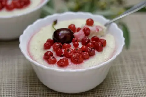 Pyszna kasza manna na mleku z wiśnią i porzeczkami, podana w białej miseczce. Idealne śniadanie lub deser.