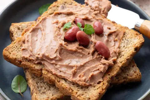 Pyszna pasta z czerwonej fasoli na chrupiących tostach, udekorowana fasolkami i listkami ziół. Idealna na śniadanie.