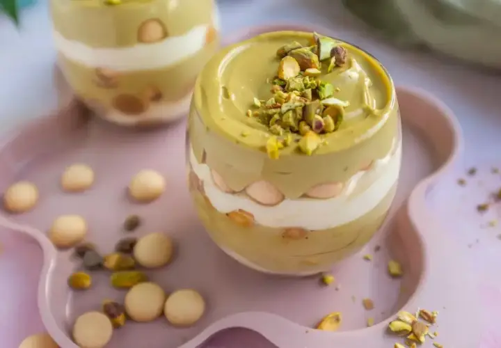 Pyszny deser w pucharku: krem pistacjowy z mascarpone, przełożony biszkoptami i posypany orzechami.