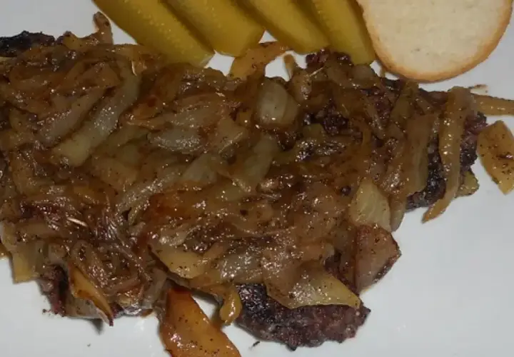 Pyszna kaszanka z patelni, duszona z cebulką, podana z ogórkiem kiszonym i kromką chleba.
