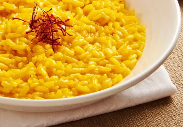 Aksamitne risotto alla milanese, złociste od szafranu, podane w białej misce, ozdobione nitkami szafranu.