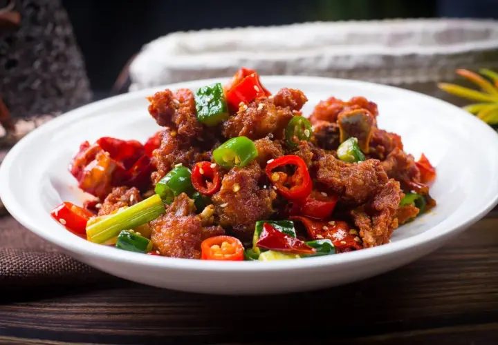 Chrupiący kurczak po kantońsku z papryczkami chili i zieloną cebulką na białym talerzu.