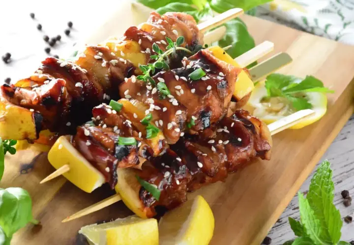 Aromatyczne yakitori z kurczaka, polane sosem teriyaki, posypane sezamem i szczypiorkiem, podane z cytryną na desce.