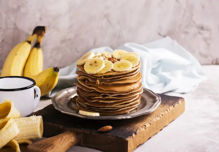 Stos naleśników z plasterkami banana i orzechami. Idealny pomysł, co zrobić z bananów na pyszne śniadanie.