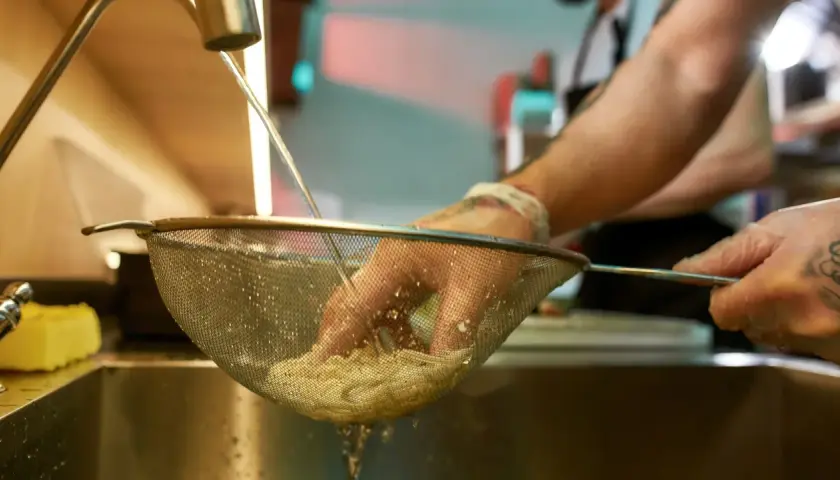 Ręce w rękawiczkach płuczą makaron pod bieżącą wodą, by zapobiec jego sklejaniu.