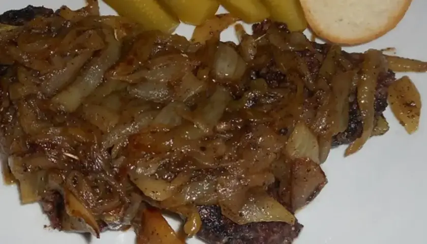 Pyszna kaszanka z patelni, duszona z cebulką, podana z ogórkiem kiszonym i kromką chleba.