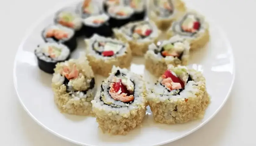 Talerz pełen pysznych roladek california sushi, posypanych sezamem. Idealne na lekki posiłek.