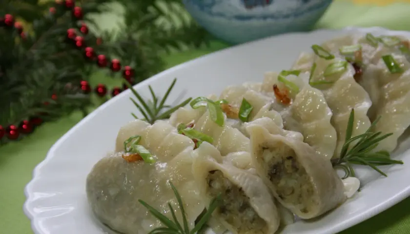 Pyszne, domowe pierogi ukraińskie, udekorowane szczypiorkiem i rozmarynem, prezentują się apetycznie na białym talerzu.