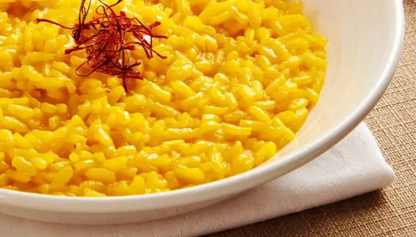 Aksamitne risotto alla milanese, złociste od szafranu, podane w białej misce, ozdobione nitkami szafranu.