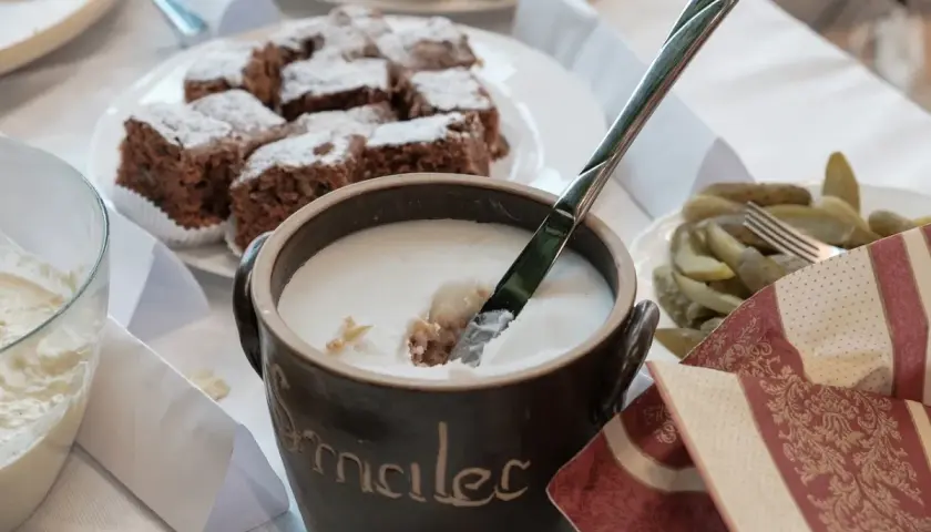 Gęsty smalec w glinianym naczyniu, obok ciasto czekoladowe i ogórki.