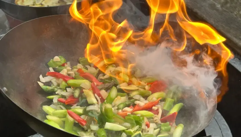 Ogień buchający z woka podczas przygotowywania pysznego stir fry z warzywami.