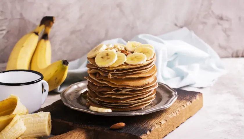 Stos naleśników z plasterkami banana i orzechami. Idealny pomysł, co zrobić z bananów na pyszne śniadanie.