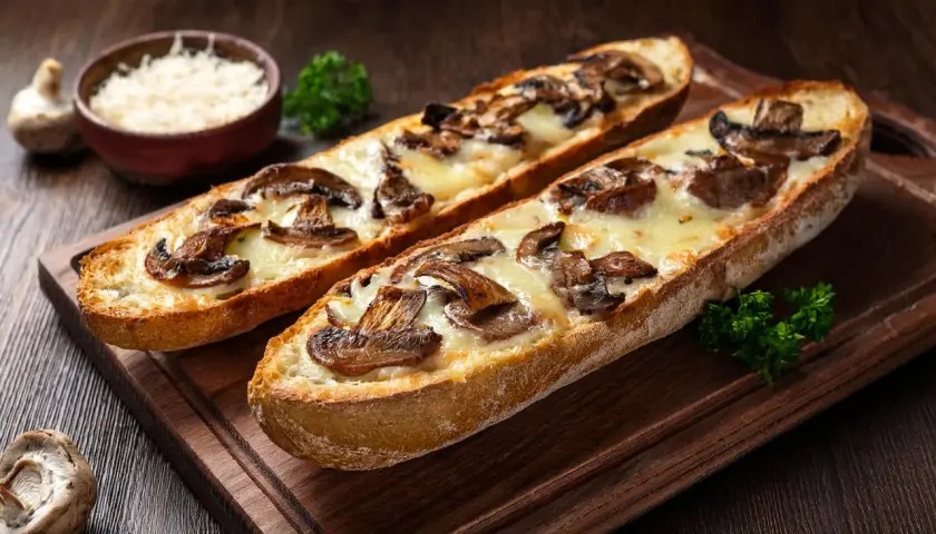 Dwie chrupiące zapiekanki z airfryer z pieczarkami i ciągnącym się serem na drewnianej desce.