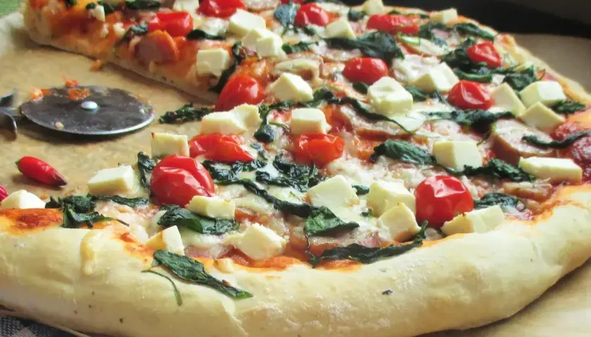 Pyszna pizza ze szpinakiem, pomidorkami koktajlowymi i kostkami sera feta. Idealna na szybki obiad.