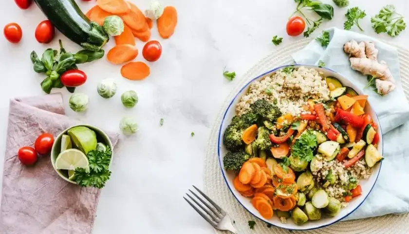 Kolorowa miska pełna warzyw i kaszy, idealna na dietę 1500 kcal. Obok świeże składniki: cukinia, marchewka, pomidorki, brukselka, limonka.