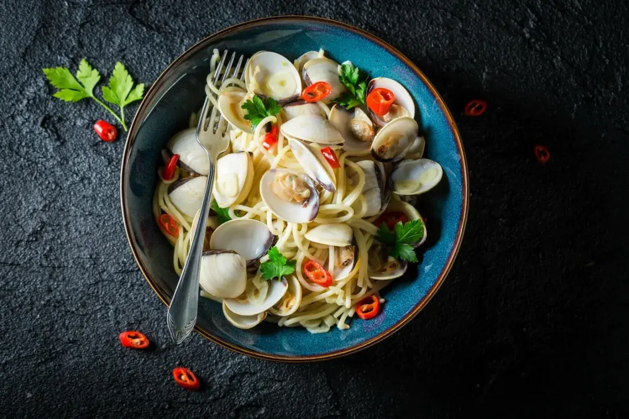 Makaron spaghetti z aromatycznymi vongole, czosnkiem i ostrą papryczką, udekorowany natką pietruszki.